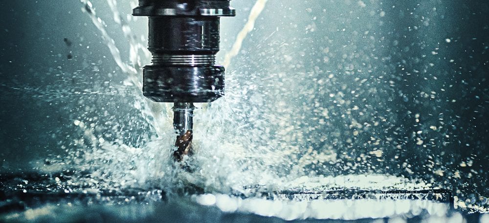 Closeup shot of a CNC machine processing a piece of metal. There are three water streams splashing the object to cool it down.